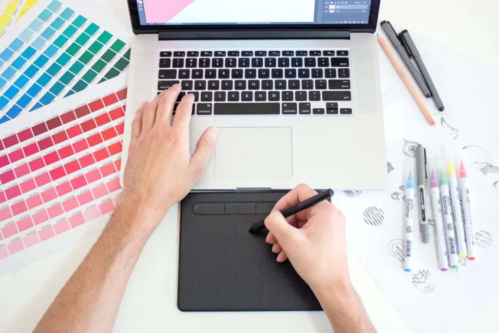 image showcasing someone using graphic design tools - 2 hands - one touching the keyboard and another is using the Wacom drawing tablet